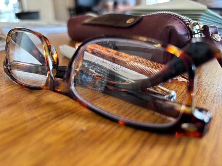 pair of glasses, pens, and a stack of letters on a table inside a café