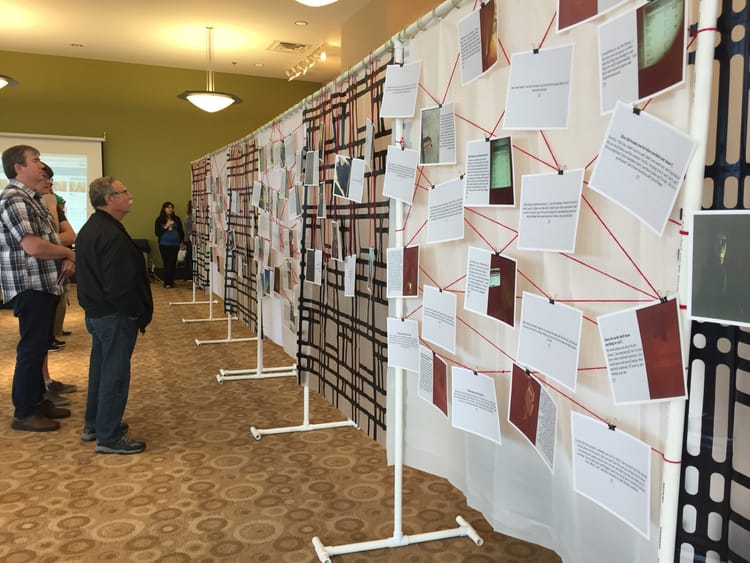 a group of people looking at a PowerPoint slides that have been printed out and hung up in a random fashion with red yard and binder clips