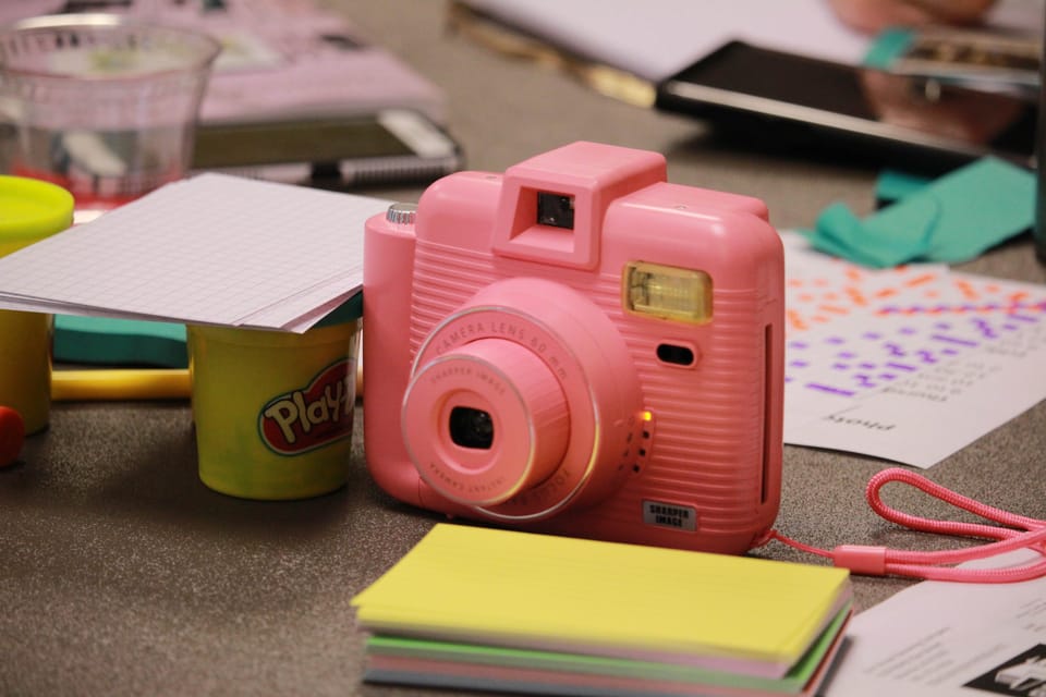 instant camera on a table with art supplies surrounding it