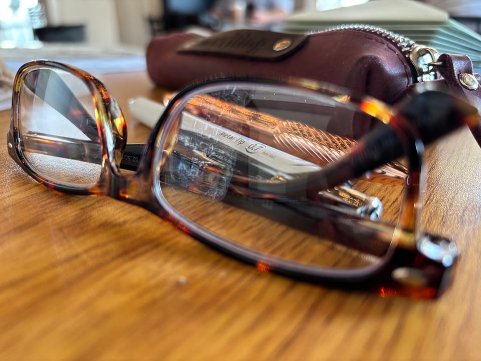 pair of glasses, pens, and a stack of letters on a table inside a café