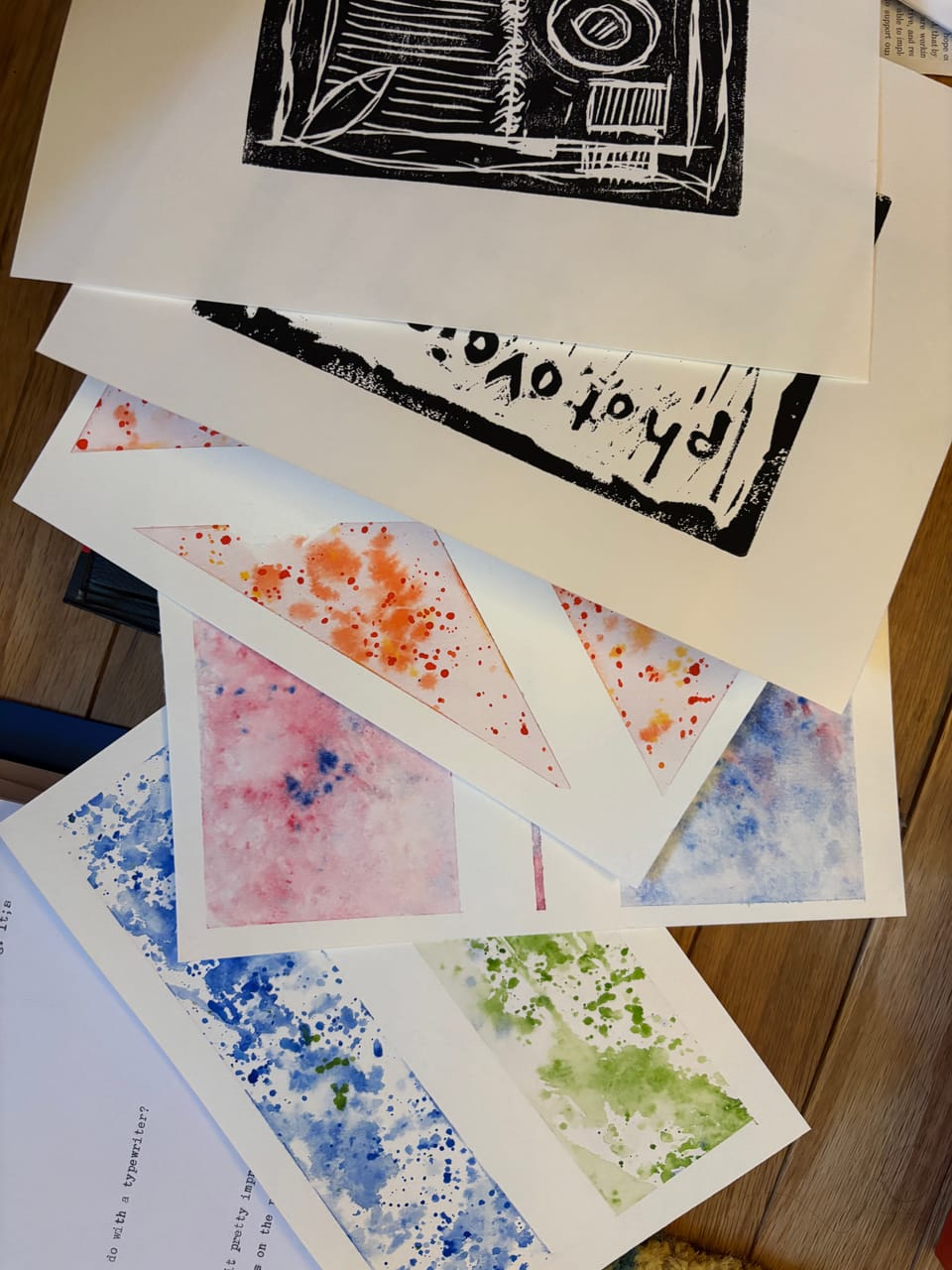 stack of various papers on the floor, some with random type, abstract watercolor, and black ink