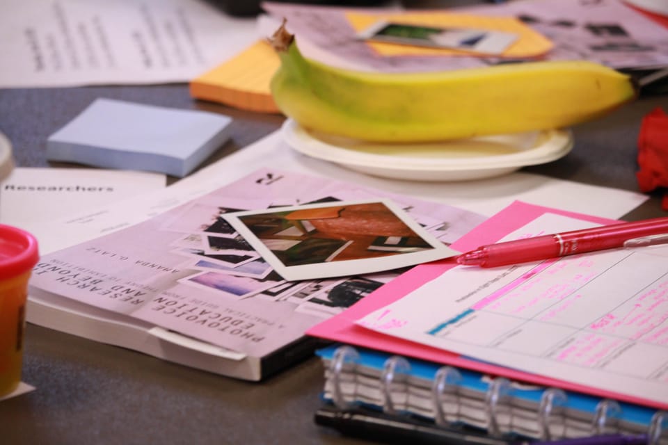 table top with books, notebooks, Polaroid photographs, and a pen